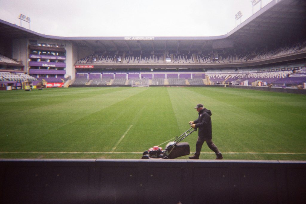 A lone groundskeeper mows a soccer field in RSC Anderlecht stadium, preparing for upcoming sports events.